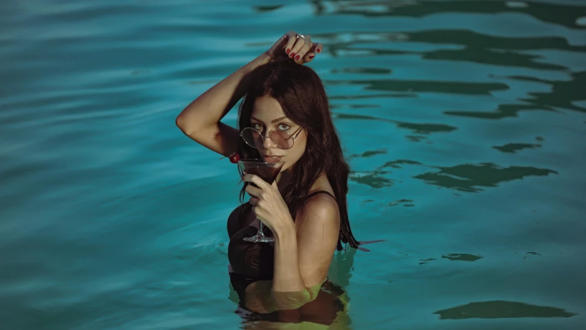 woman in wetsuit holding up a beer standing in water