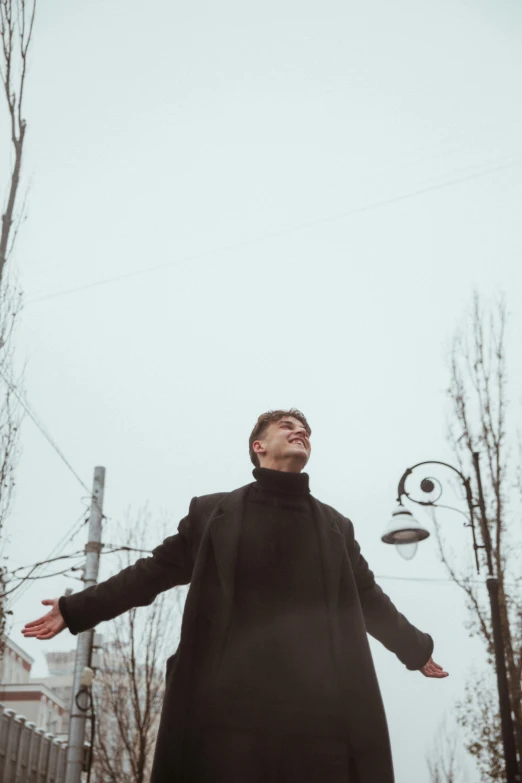 man in long black coat throwing frisbee near tree