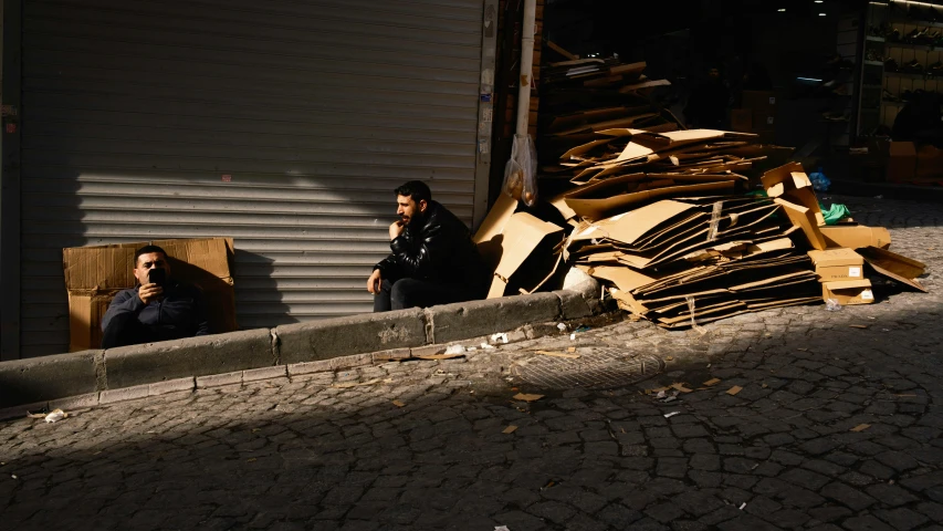 a man sitting on a curb by a pile of wood