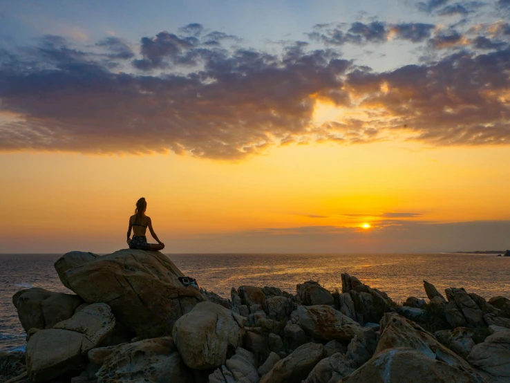 woman sitting on a rock near the ocean during sunset