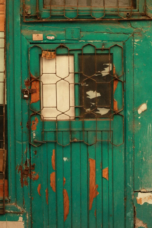 an old, green wall with stained glass and a rusty metal barred window