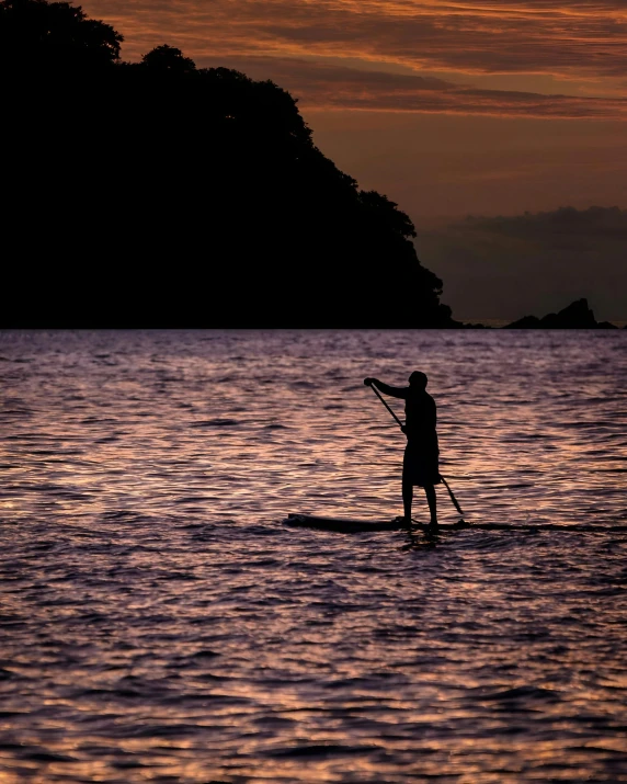 an image of a person riding a paddle board at sunset