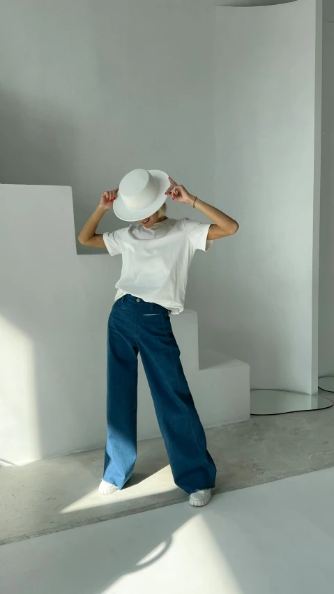 a woman poses in a white t - shirt and wide jeans