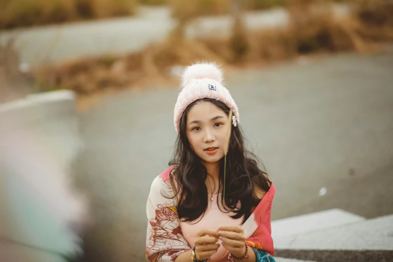 a girl is sitting and holding her hand under her hat