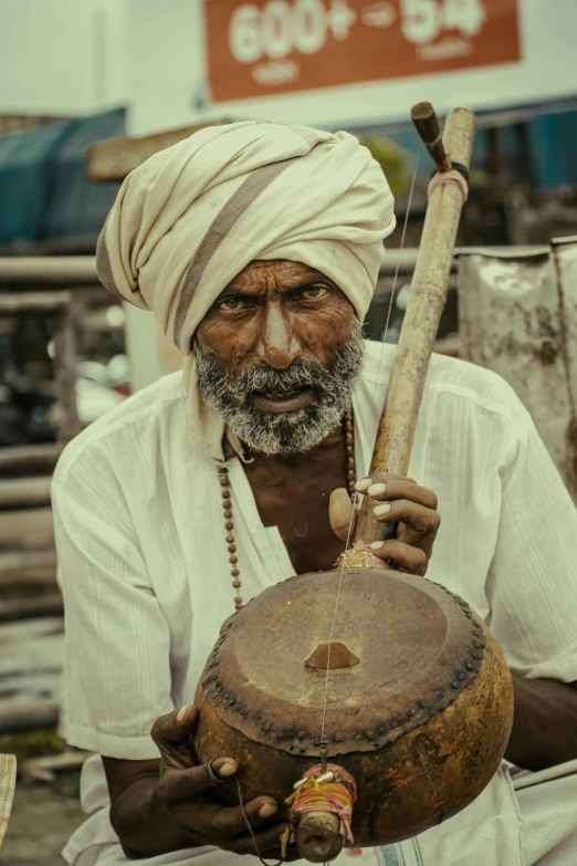 an old man with long turban holding a drum