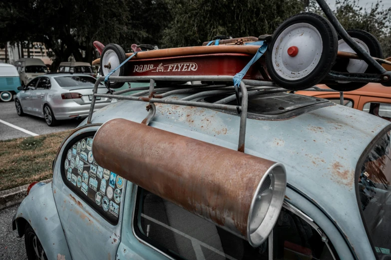 a small, rusty car sits on the street while an orange and blue car is parked