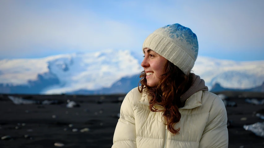 a young woman stands with a snow - capped mountain behind her