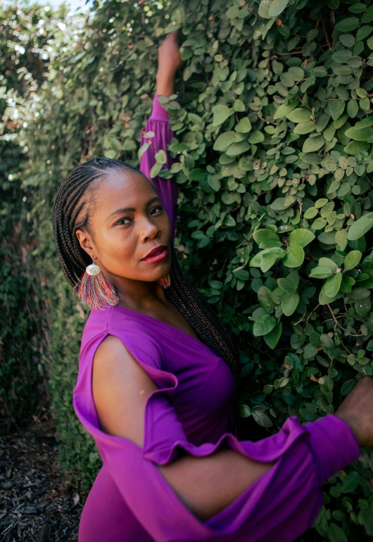 a black woman in purple poses with her hand on the wall