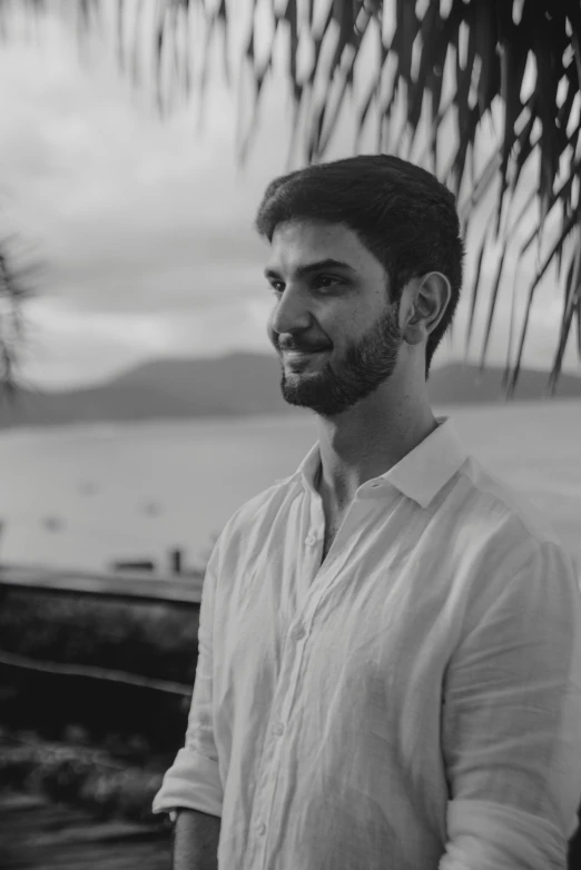 a man standing next to the ocean in front of a tree