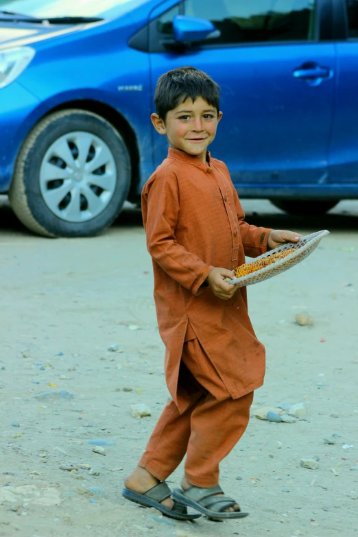 a small boy holding a plate of food next to a car