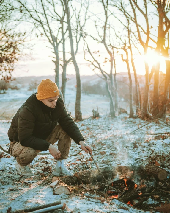 a man sitting in front of a camp fire with snow on it