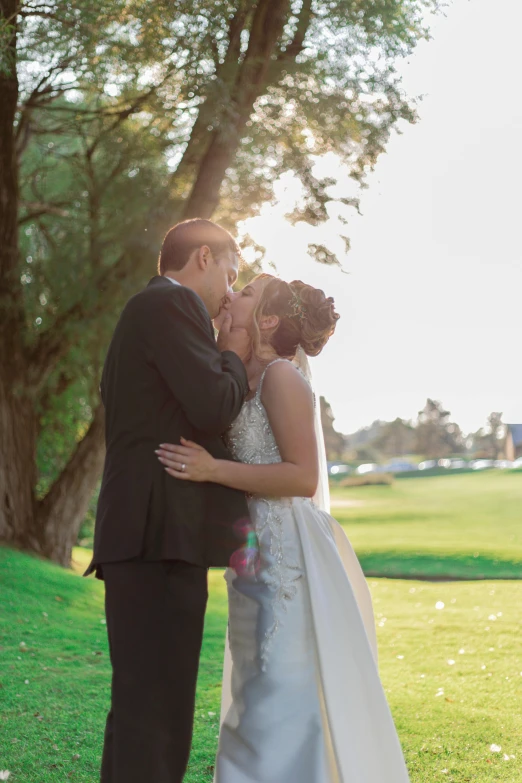 a bride and groom are kissing in front of a tree