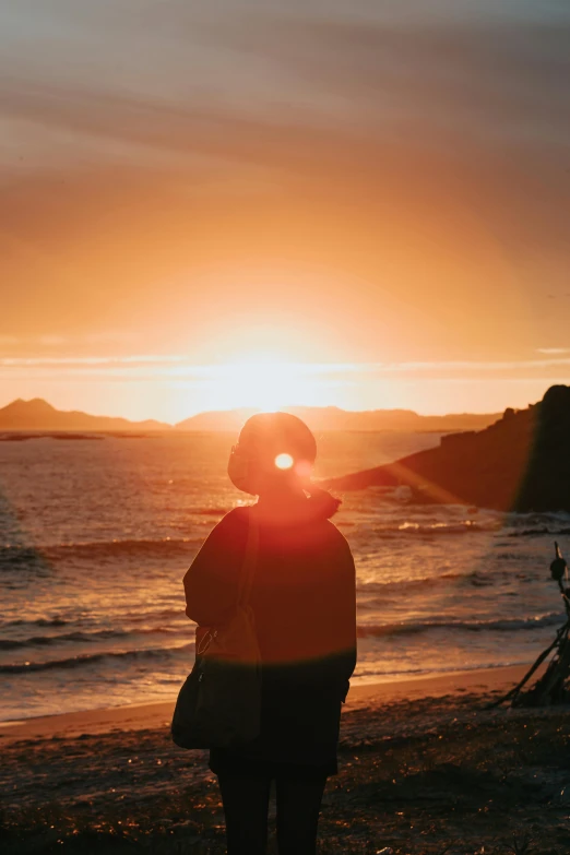 woman on beach during sunset with her camera lens up