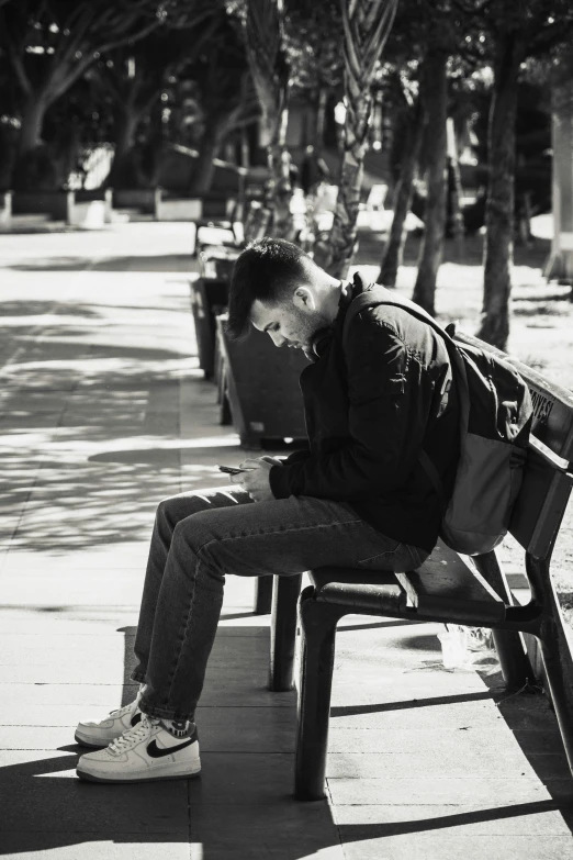 a black and white po of a man with a backpack sitting on a bench