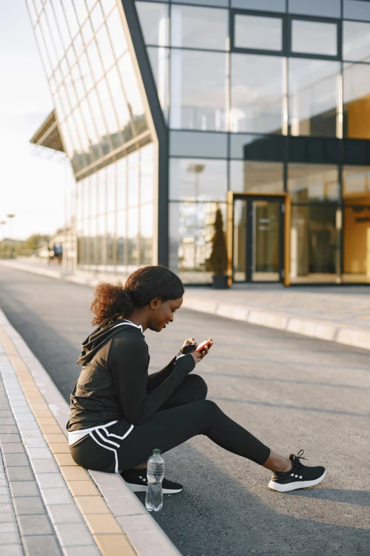 a  with curly hair sits in front of a building on her cell phone