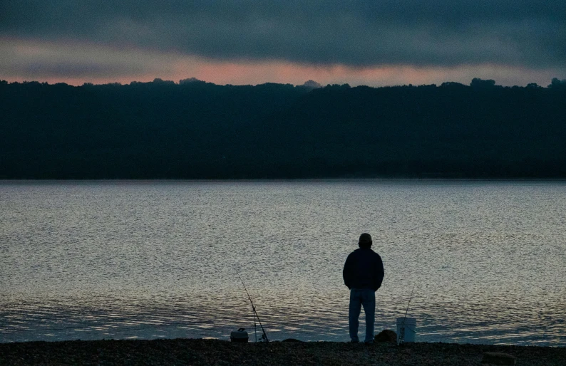 a man standing on the shore of a lake watching the sunset