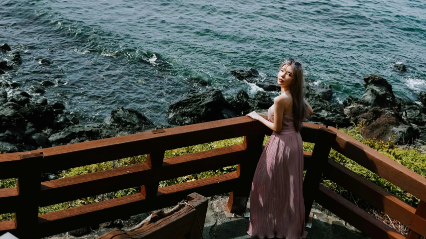 the girl standing by the fence looks over the water