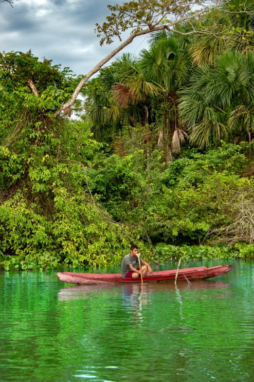 a man paddles a red canoe in clear water