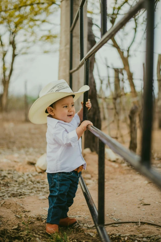 a child with a cowboy hat is standing next to a metal fence