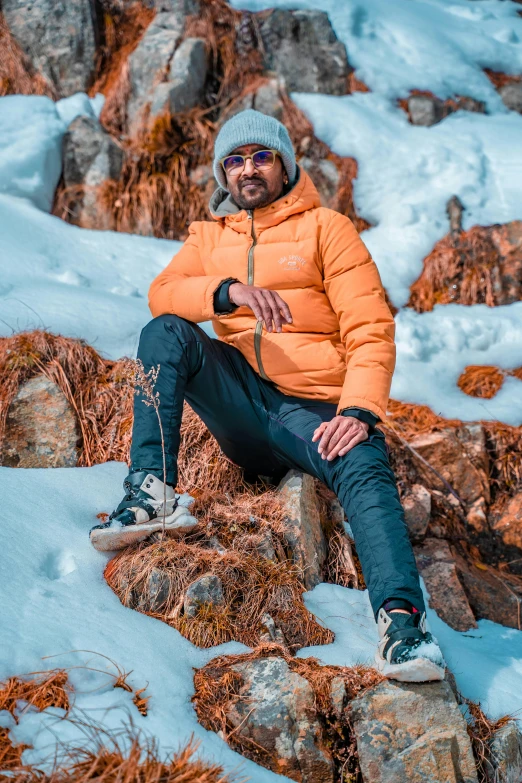 a man in orange jacket and blue pants sitting on rock