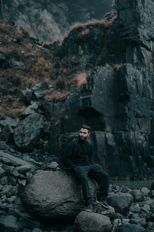 a man sitting on some rocks wearing a black jacket