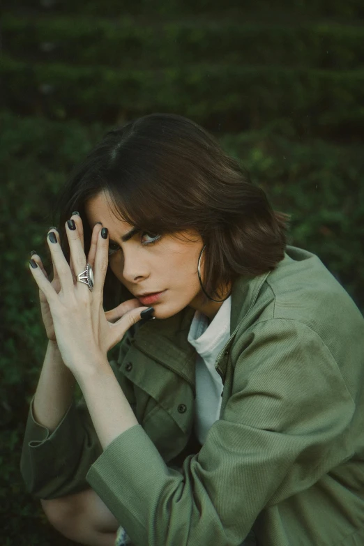 a woman in green jacket holding her hand on top of her finger