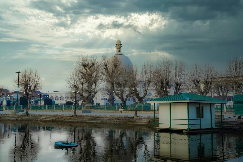 a pond in the middle of a city with some trees and a small building in the background