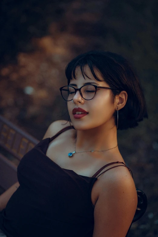 the girl with black glasses is sitting by a bench