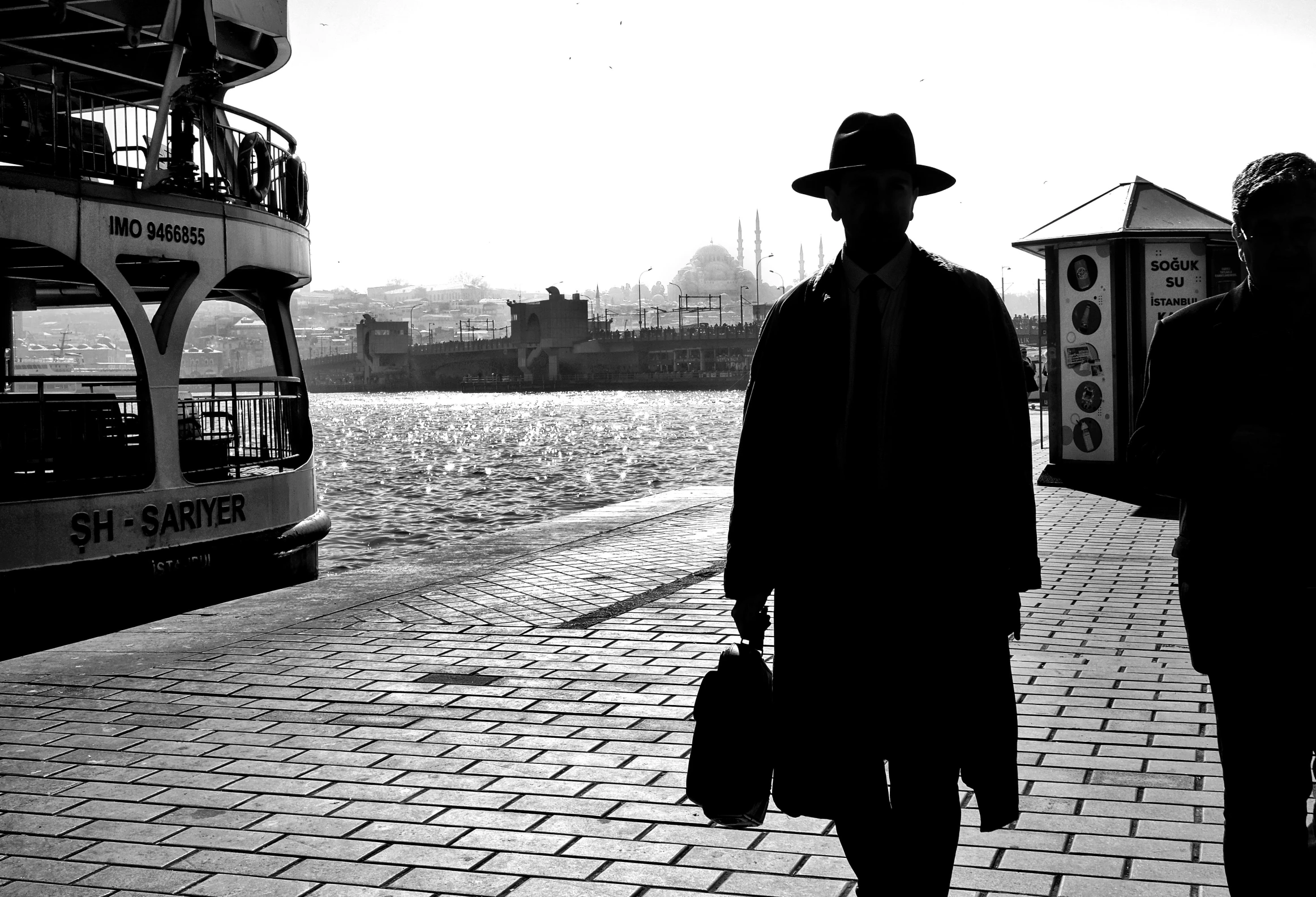 a silhouette of a man holding a small bag and wearing a hat