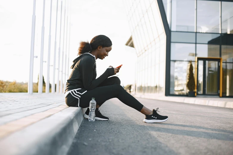 a young woman in athletic wear is sitting on the ground looking at her cell phone