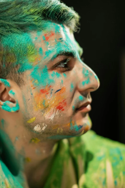 a man with green and blue hair has splotters of colored powder on his face