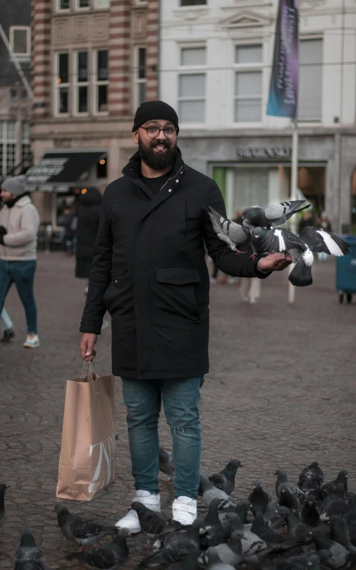 man in black coat holding bag and pigeons in foreground
