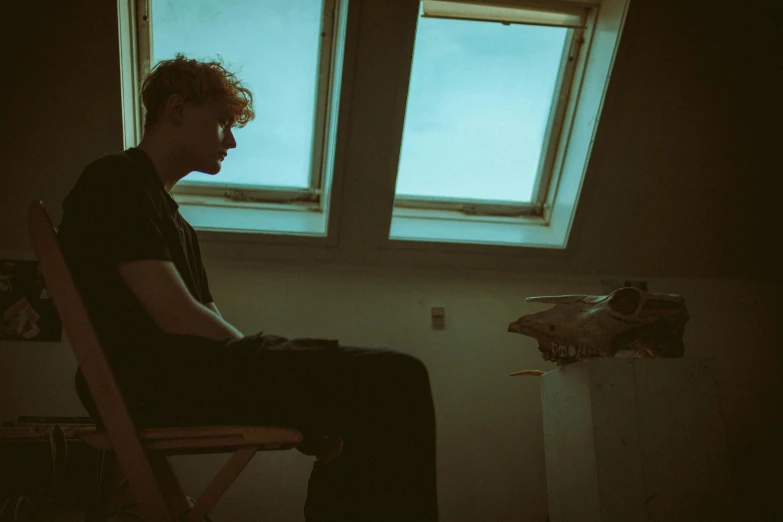 a young man sitting in a chair next to a window