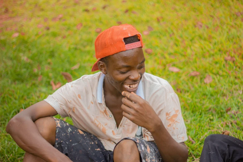 a man sitting on a grass field wearing an orange hat