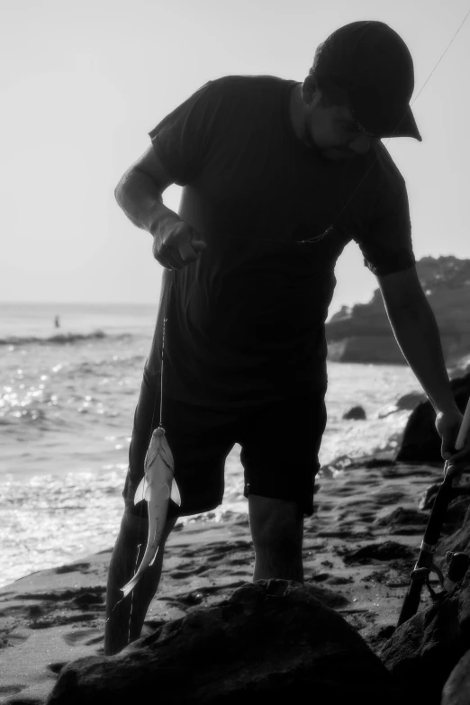 the man is standing on the rocky beach with a stick