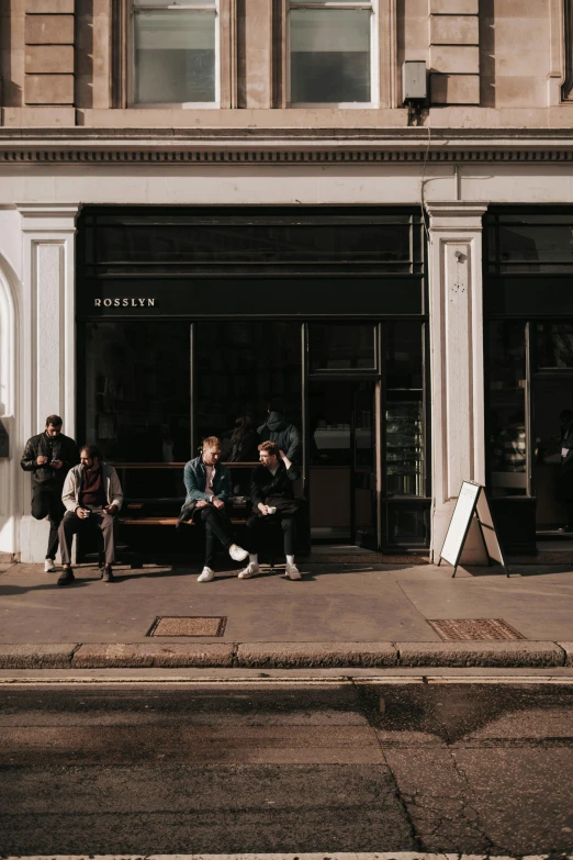 people sit and talk on the sidewalk in front of a building