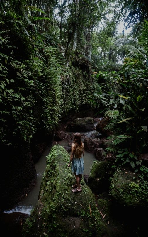 a woman in a black shirt standing on rocks next to a forest