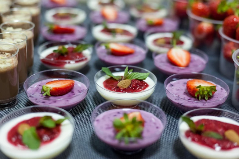 several dishes filled with strawberry desserts and cups filled with various toppings