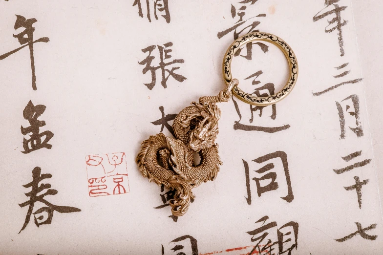 a small gold - toned key ring lies on a fabric with chinese characters