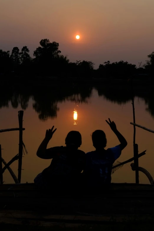 a couple sitting on a bench at a lake watching the sunset