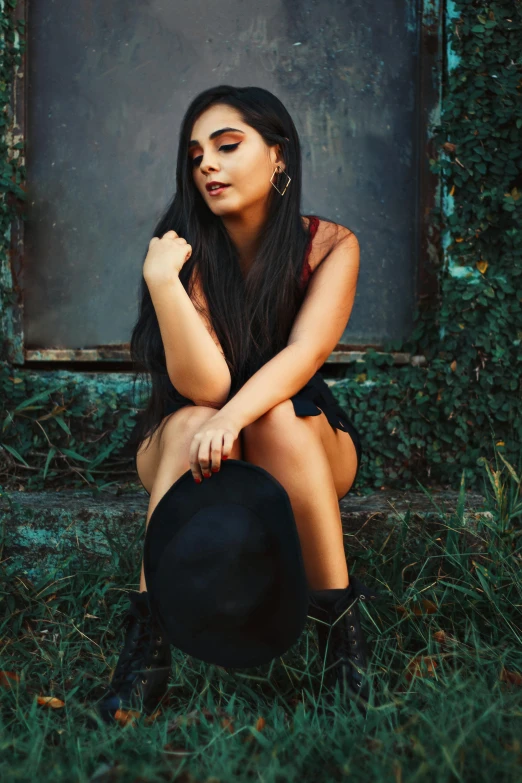 a woman in black clothes and hat sitting on a ground