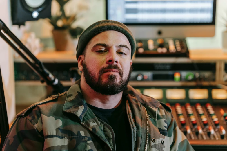 a man wearing a jacket and a beanie is sitting in a recording room with his eyes closed