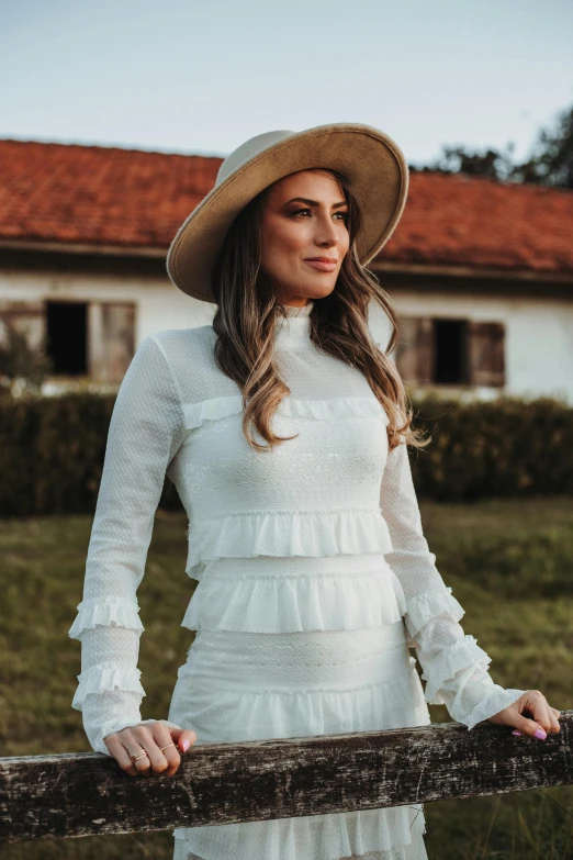 a woman in a hat is leaning on a fence