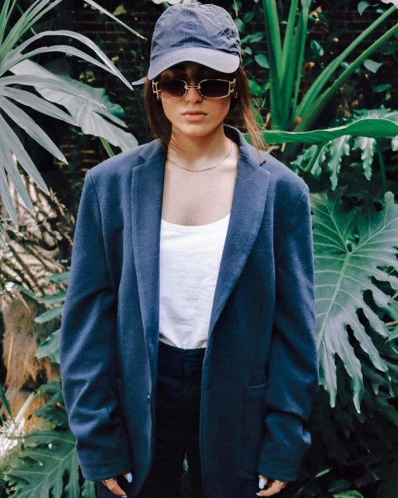 a young lady with sunglasses and a hat is standing in front of plants