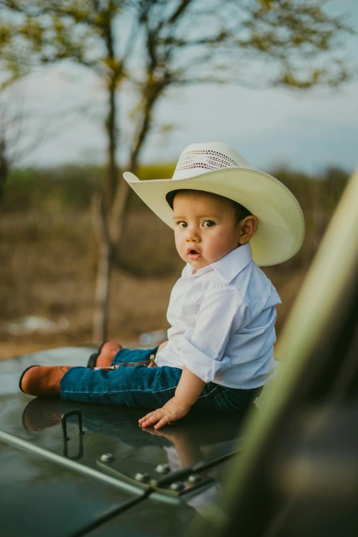 a little boy in a white hat sitting on top of a car