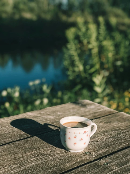 a coffee cup on a wooden table near the water