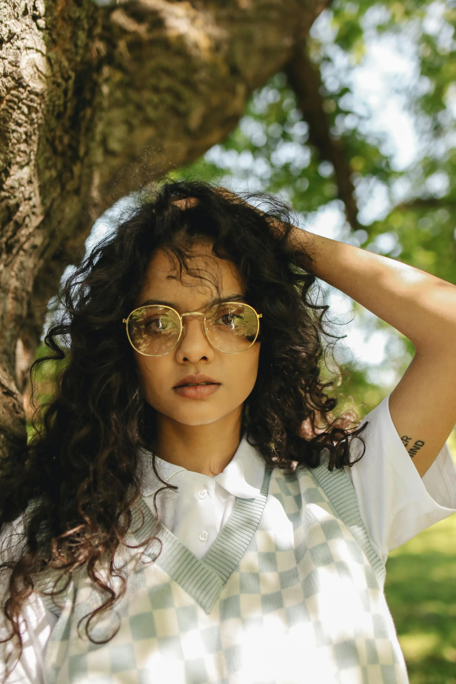 woman in checkered shirt and gold glasses standing against tree