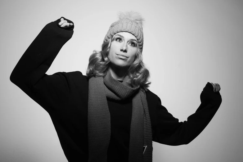 a woman in winter clothes, knit hat and scarf posing with her fist up