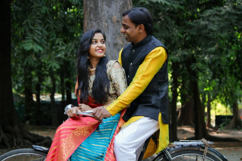 a couple are sitting on a bicycle with some trees in the background