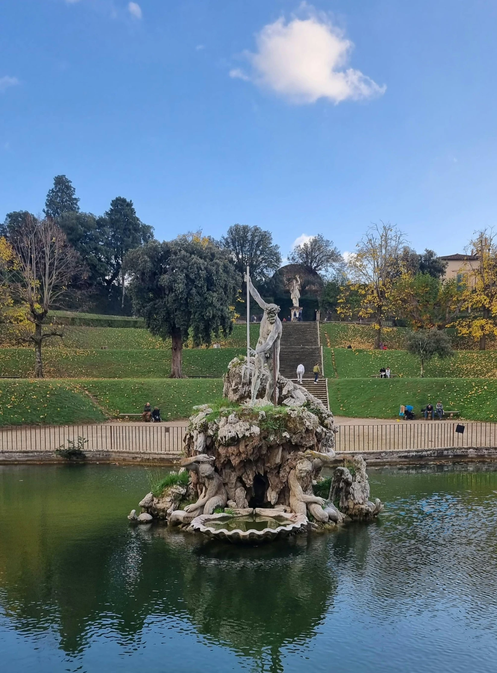 a statue in a pond with people walking by